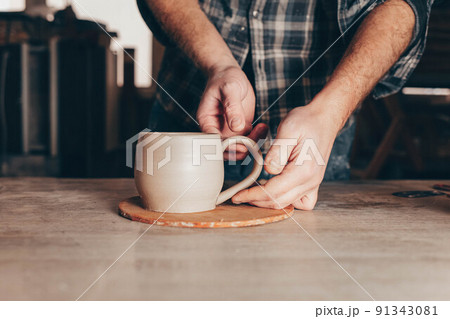 Potter glues ears to a cup. Process of creating a ceramic cup. 91343081