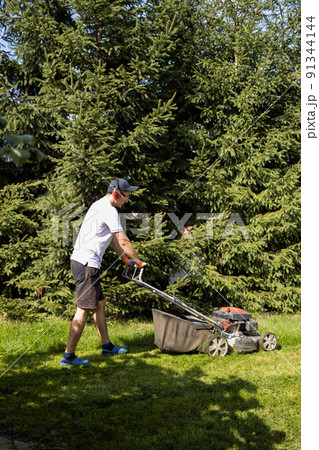 Gardener mowing the grass with a gasoline lawn mower 91344144