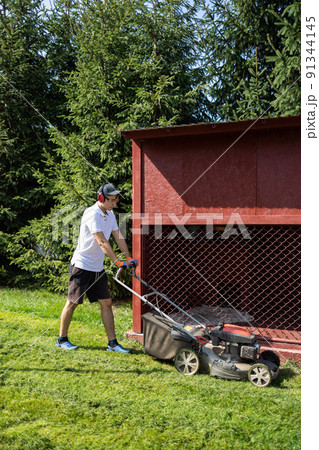 Gardener mowing the grass with a gasoline lawn mower 91344145