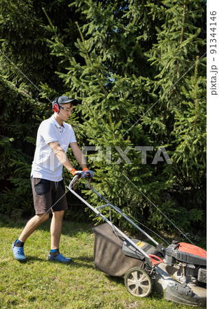 Gardener mowing the grass with a gasoline lawn mower 91344146