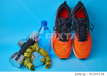 Orange sneakers, dumbbells, measuring tape and plastic drinking water bottle on a blue background 91344148