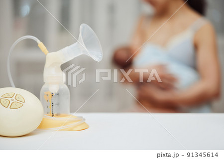 breast pump with breast milk against the background of a mother holding child. breast pump with breast milk against the background of a mother holding child. 91345614