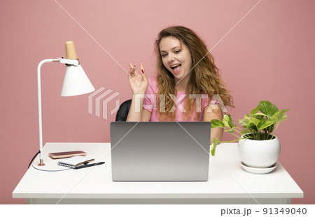 Happy young freelancer curly woman in a blue t-shirt working with a laptop computer and speaking with a client or friends with messengers. Working on a project. Freelance worker. 91349040