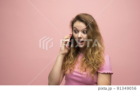 Happy surprised shocked young pretty woman speaking with a phone over pink wall background. Using mobile phone. Happy surprised shocked young pretty woman speaking with a phone over pink wall background. Using mobile phone. 91349056