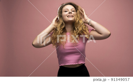 Young woman listening music in headphones and dancing with a smile face and stand over pink background. Attractive lady enjoying song copy space. 91349057