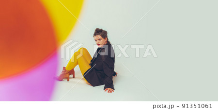 Film effect. Portrait of young stylish girl in yellow tight and black jacket posing isolated over grey studio background 91351061