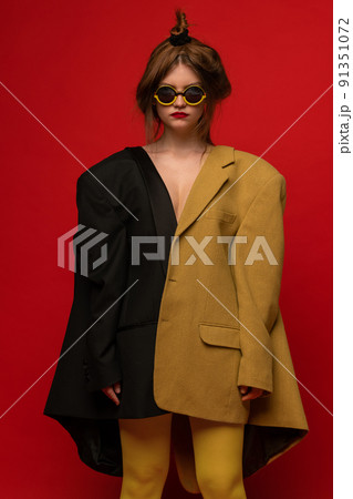 Stylish portrait of young girl wearing two oversized jackets, stylish extravagant glasses, posing isolated over red background Stylish portrait of young girl wearing two oversized jackets, stylish extravagant glasses, posing isolated over red background 91351072