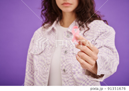 Close-up of young woman holding cancer awareness ribbon against purple background Close-up of young woman holding cancer awareness ribbon against purple background 91351676