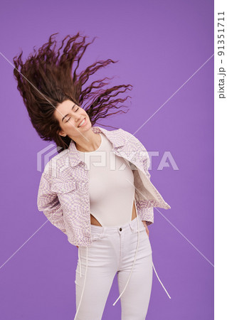 Happy young girl waving her head with long curly hair and smiling standing against purple background Happy young girl waving her head with long curly hair and smiling standing against purple background 91351711