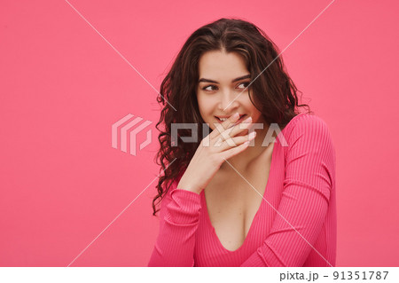 Portrait of funny young woman closed her mouth with hand while smiling against the pink background Portrait of funny young woman closed her mouth with hand while smiling against the pink background 91351787