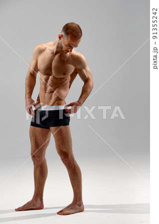 Young male athlete posing. Handsome athletic male power guy. Fitness muscular person. Young athlete showing muscles in the studio, posing shirtless on gray background. 91355242