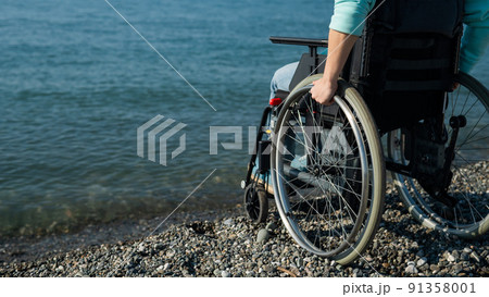 Caucasian woman in a wheelchair on the seashore. Close-up of female hands. Caucasian woman in a wheelchair on the seashore. Close-up of female hands. 91358001