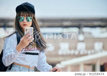 別府駅前でスマホを持って観光する若い女性 91358474