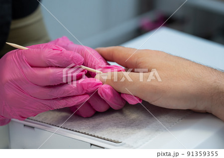 Manicurist removes cuticles with an orange stick to a male client.  91359355