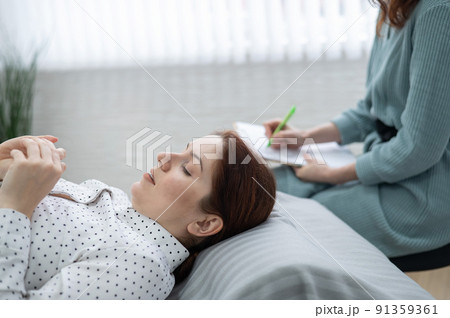 A caucasian woman lies on a couch and expresses her feelings, while a psychologist makes notes on a tablet.  91359361
