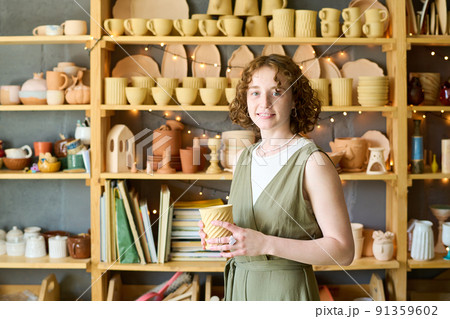 Young successful owner of small shop with handmade clay mug in hands Young successful owner of small shop with handmade clay mug in hands 91359602