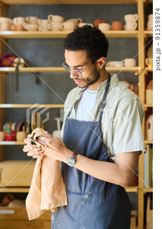 Young multi-ethnic craftsman in apron wiping his hands with towel 91359874