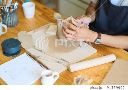 Hands of young male potter forming shape of vase or jug by his workplace 91359902