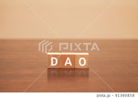 DAOの文字。分散型自律組織。3つの木製ブロックに書かれている。白い文字。木製テーブルの背景。 91360858