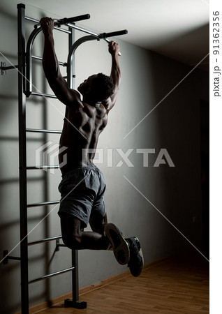 African american man with naked torso pulls up on horizontal bar in gym. African american man with naked torso pulls up on horizontal bar in gym. 91362356