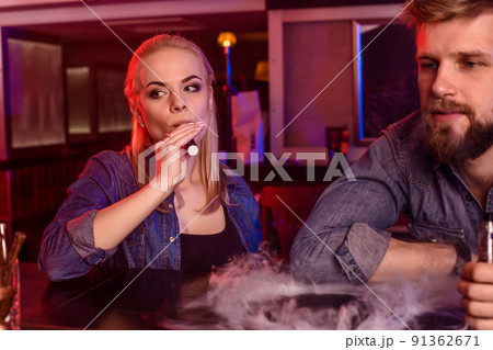 A man and woman smoking electronic cigarette in a vape bar. 91362671