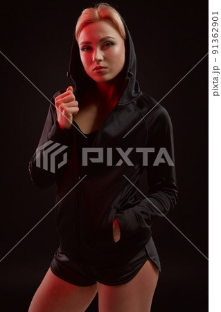 Beautiful seductive sporty girl with the slim sexy figure in the black hoodie, sport underwear and little black shorts is posing in the studio 91362901