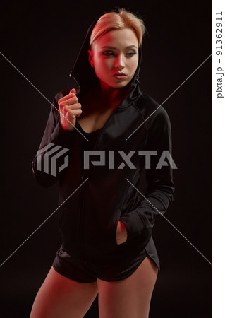 Beautiful seductive sporty girl with the slim sexy figure in the black hoodie, sport underwear and little black shorts is posing in the studio 91362911