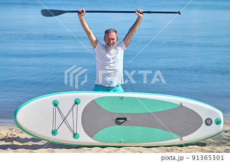 Man with raised paddle standing behind rowing board Man with raised paddle standing behind rowing board 91365301