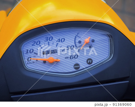 A speedometer with a dial and orange hands is located on the handlebars of a yellow-black motorcycle. Closeup photo A speedometer with a dial and orange hands is located on the handlebars of a yellow-black motorcycle. Closeup photo 91369060
