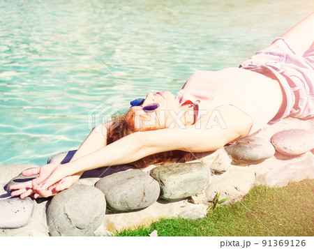 A fair-haired woman lies on the stone side of a turquoise pool under the bright summer sun. High key A fair-haired woman lies on the stone side of a turquoise pool under the bright summer sun. High key 91369126