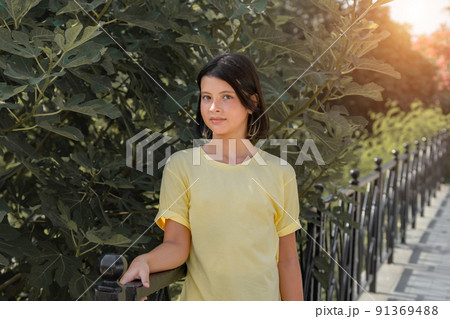 Portrait of a young girl standing near a metal fence. 91369488