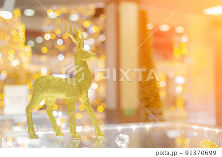 A golden shiny Christmas deer stands on a glass surface in a bright bokeh background. Selective focus. A golden shiny Christmas deer stands on a glass surface in a bright bokeh background. Selective focus. 91370699