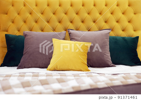 Multi-colored square pillows lie on the bed with a soft yellow velvet headboard with capitones. Selective focus. 91371461