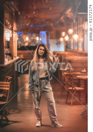 A woman stands inside an evening deserted luminous cafe with a wooden interior. Blurred image 91372174