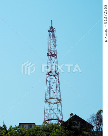 A tall cell tower rises above the rooftops of private houses against a blue sky. Selective focus A tall cell tower rises above the rooftops of private houses against a blue sky. Selective focus 91372568