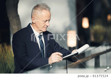 Serious senior gray-haired businessman in stylish suit standing at railing in convention center and looking through business papers while preparing for speech Serious senior gray-haired businessman in stylish suit standing at railing in convention center and looking through business papers while preparing for speech 91375524