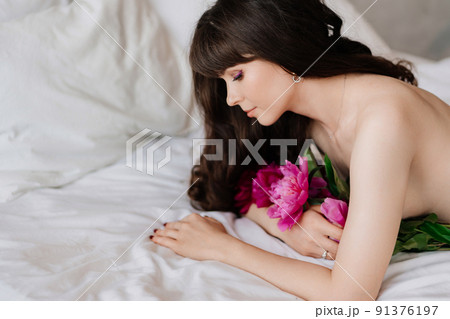 topless. an attractive and sexy woman with a bouquet of peonies lies in bed. 91376197