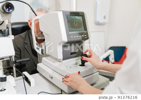 doctor examines elderly man's eye on screen of autorefractometer.  91376216