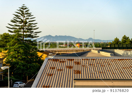 View of an urban landscape with a road, a large tree and the mountains in the background. View of an urban landscape with a road, a large tree and the mountains in the background. 91376820