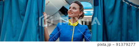 Joyful woman stewardess holding curtains in passenger aircraft Joyful woman stewardess holding curtains in passenger aircraft 91379277