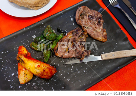 Baked lamb leg slices with potato wedges and padron peppers on slate board 91384683