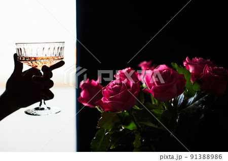Woman holds a glass of champagne in her hand, next to it is a bouquet of flowers made of roses. The concept of a gift and congratulations. Front view. Woman holds a glass of champagne in her hand, next to it is a bouquet of flowers made of roses. The concept of a gift and congratulations. Front view. 91388986