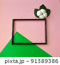 Summer modern composition. Black photo frame, green leaves and flower cotton of tree on pastel pink background. Flat lay, top view, copy space 91389386