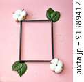 Summer modern composition. Black photo frame, green leaves and flower cotton of tree on pastel pink background. Flat lay, top view, copy space 91389412
