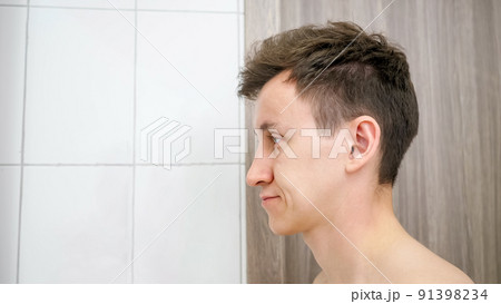 Sleepy man stands in bathroom rubbing eyes. 91398234