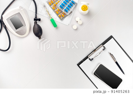 Top view of doctor's desk table, blank paper on clipboard with pen, electronic manometer to measure the blood pressure. 91405263
