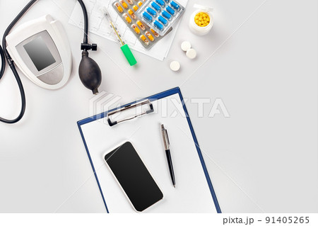 Top view of doctor's desk table, blank paper on clipboard with pen, electronic manometer to measure the blood pressure. 91405265