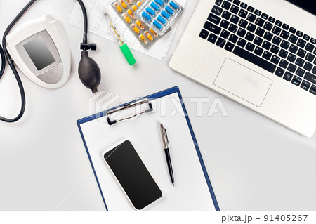 Top view of doctor's desk table, blank paper on clipboard with pen, electronic manometer to measure the blood pressure. 91405267