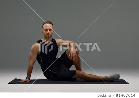 Confident young fitness man exercising on a fitness mat indoors, over gray wall background Confident young fitness man exercising on a fitness mat indoors, over gray wall background 91407614