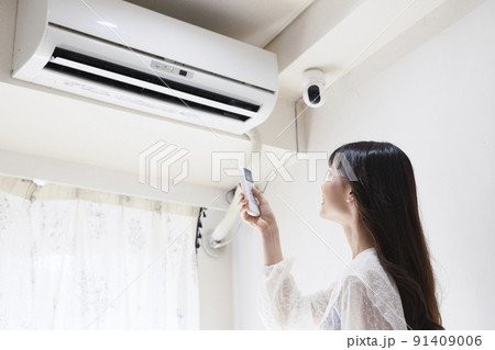 エアコンのスイッチを入れる女性 91409006